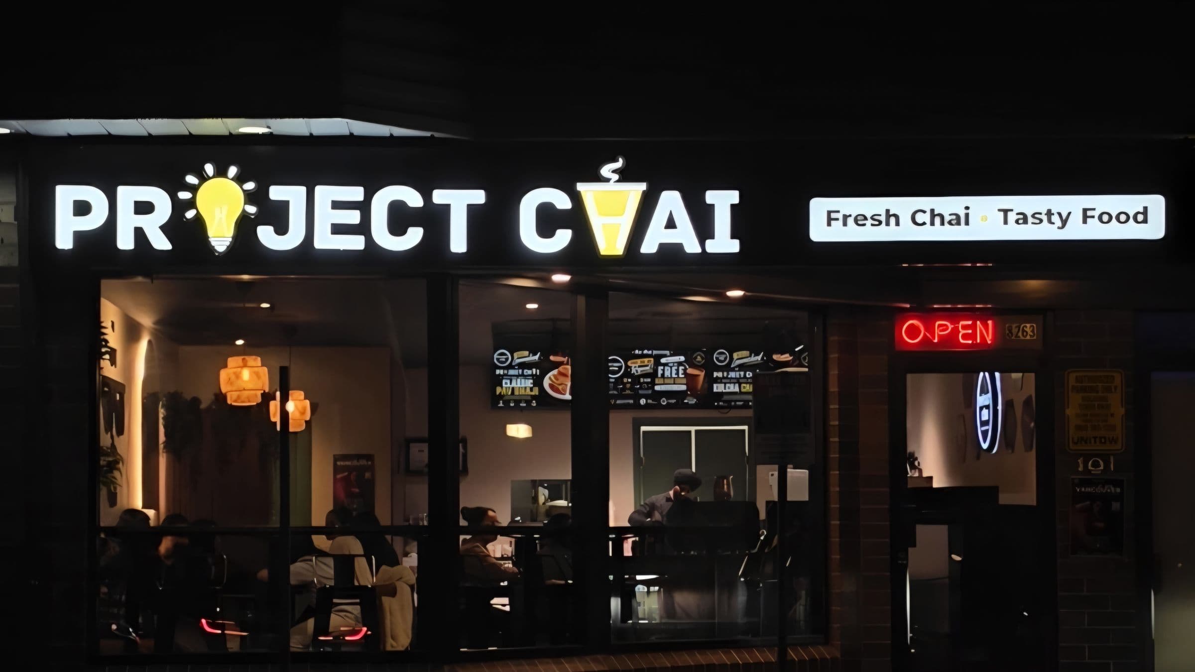 Project Chai at night, seen from the street: the lit sign, the tagline board, the OPEN sign and the door at 8263.